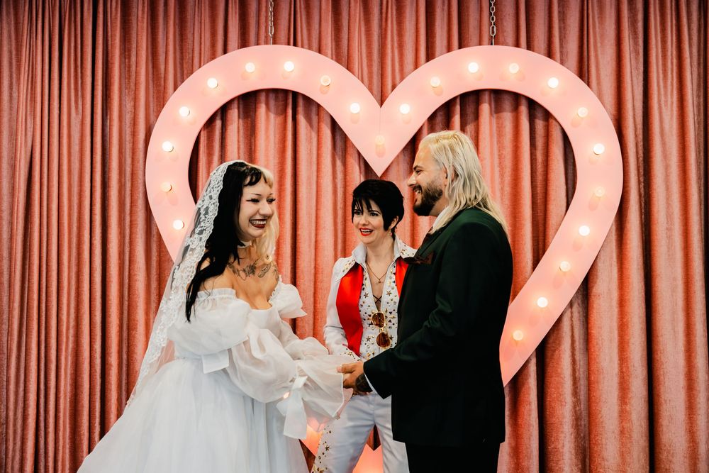 Couple exchanging vows before lit heart backdrop with Elvis officiant at Las Vegas wedding.