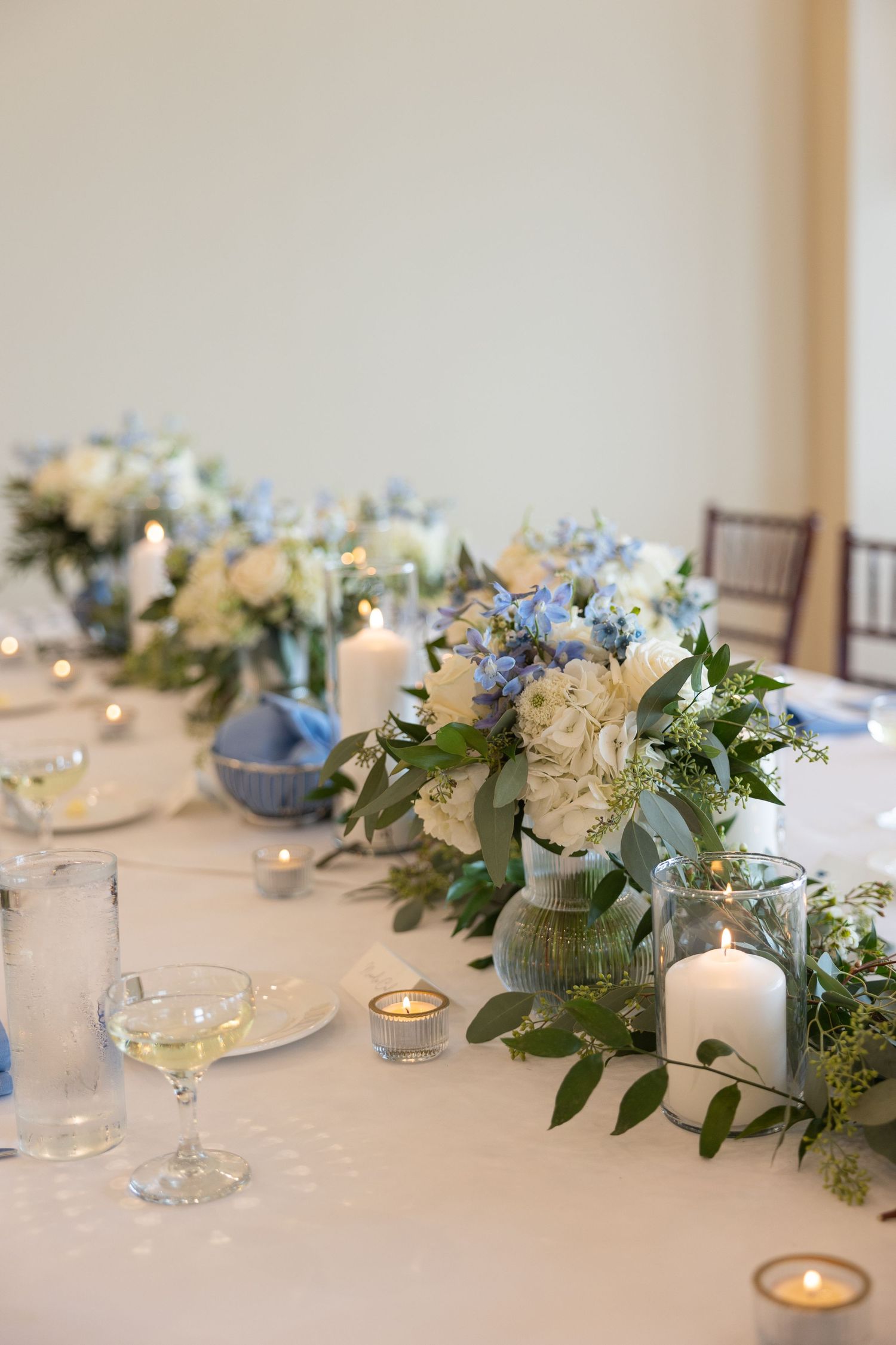 Elegant table setting with blue and white flowers in mason jars, candles and greenery garland creating a romantic centerpiece.