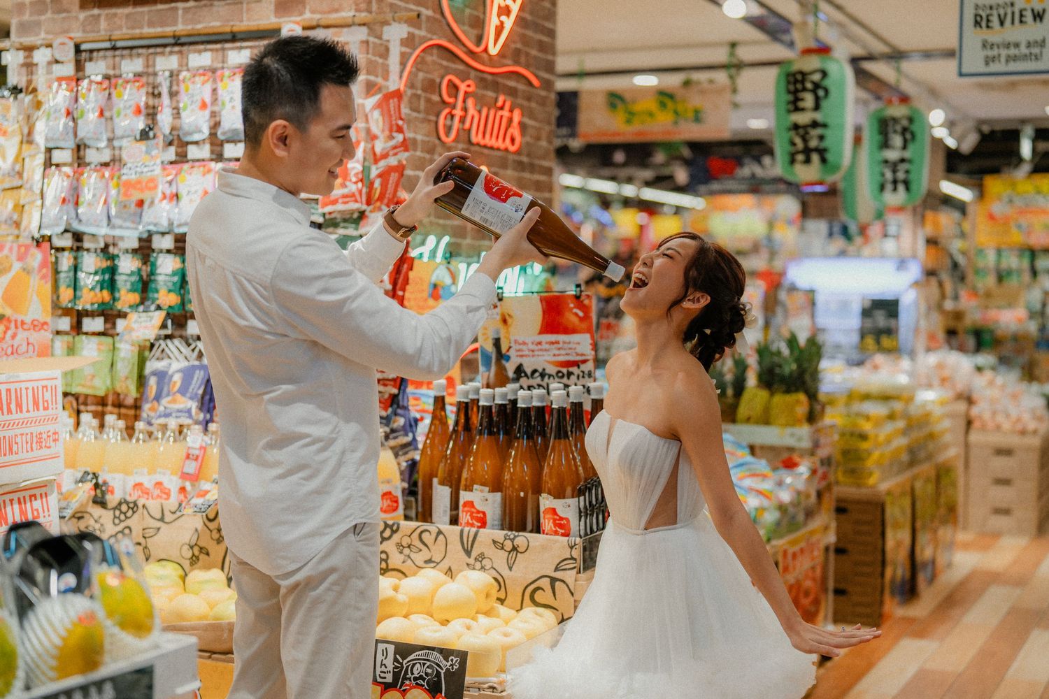 Newlyweds in white share drinks together in front of store shelves.