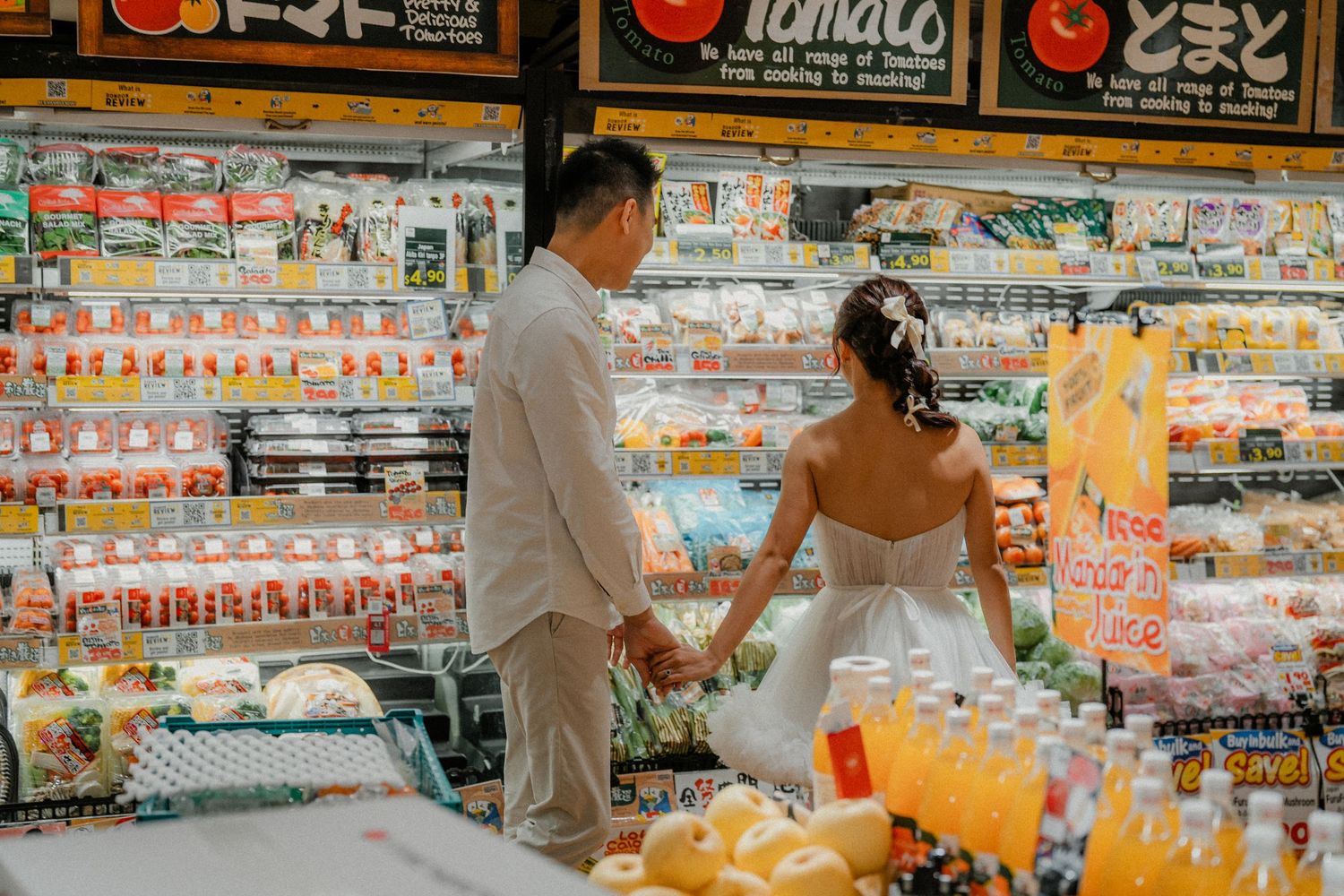 Couple in white outfits posing playfully in a grocery store aisle with vibrant product displays.