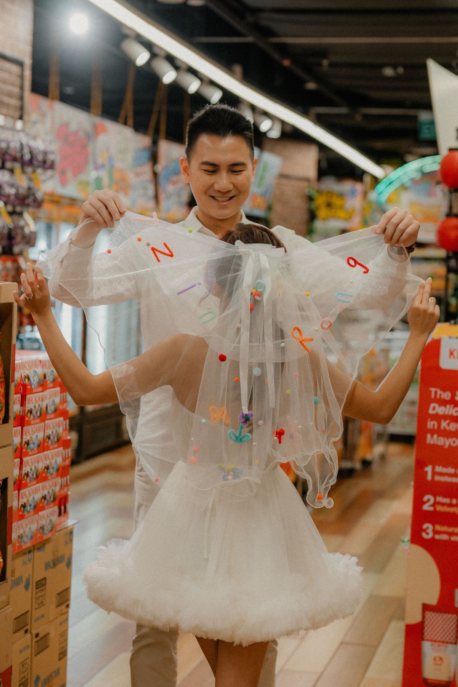 A person in white clothing holds plastic bags while wearing a tulle skirt in a store.