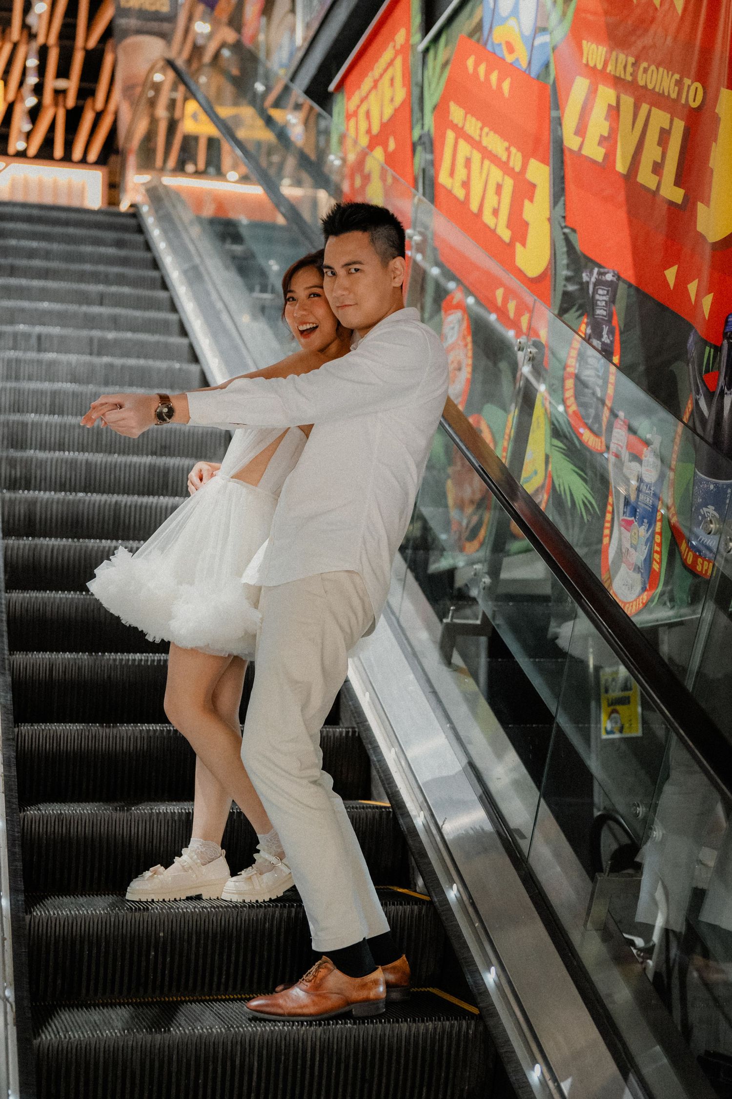 A stylish couple poses on an escalator in matching white outfits.