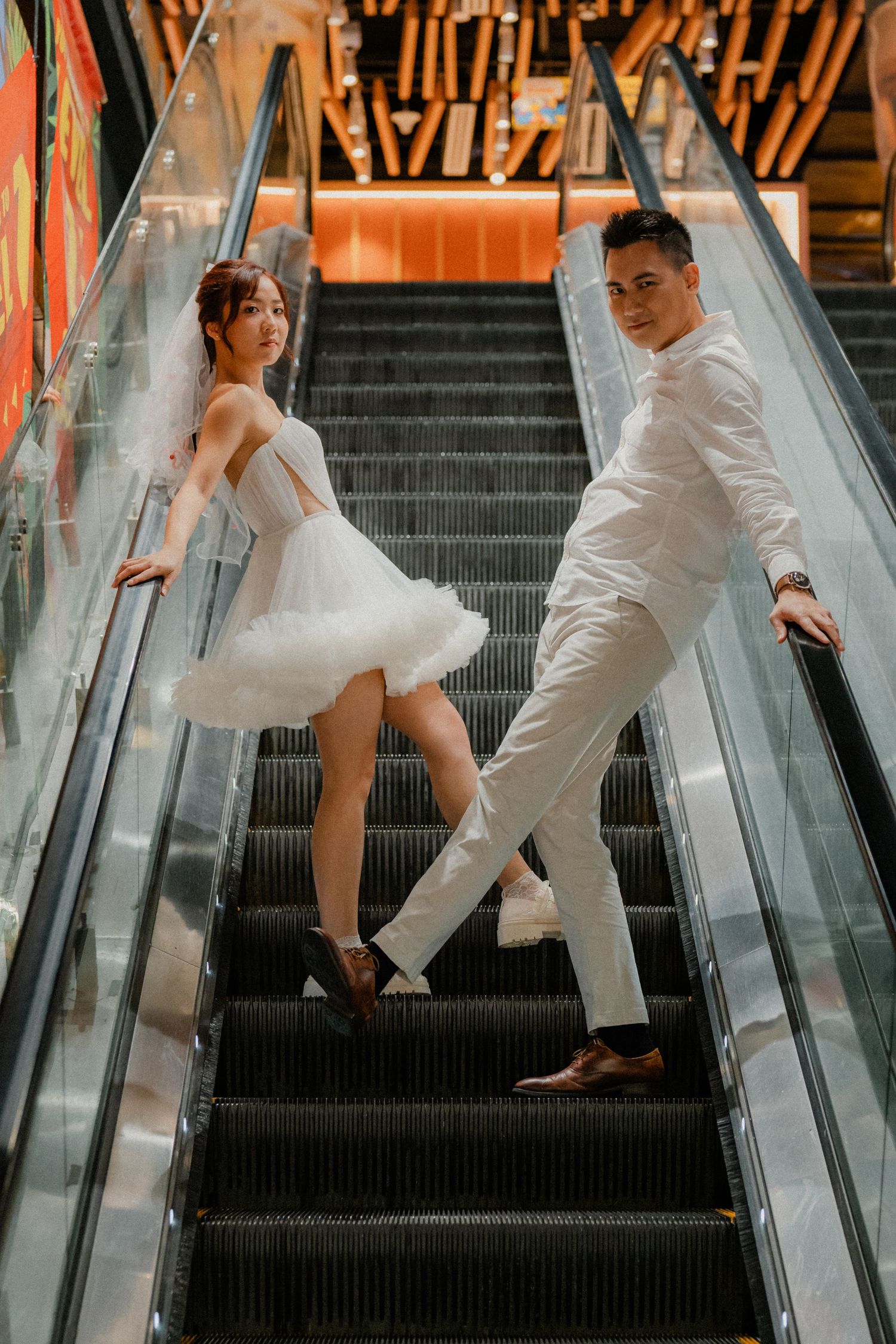 Couple in white outfits poses on escalator steps in dramatic photo sequence.
