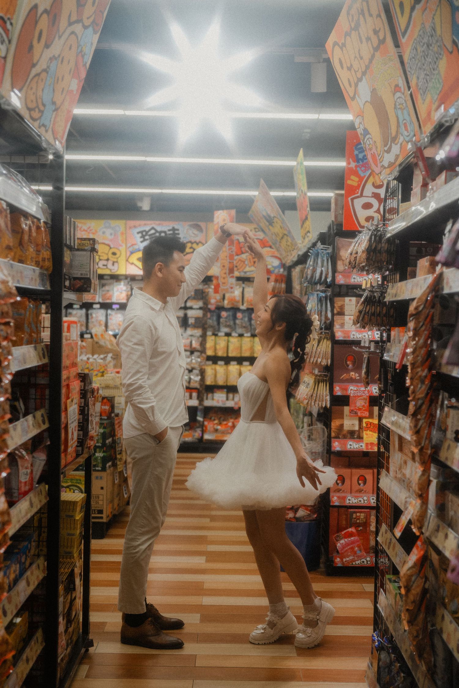 A playful couple in white attire dances in a snack food aisle of a grocery store.