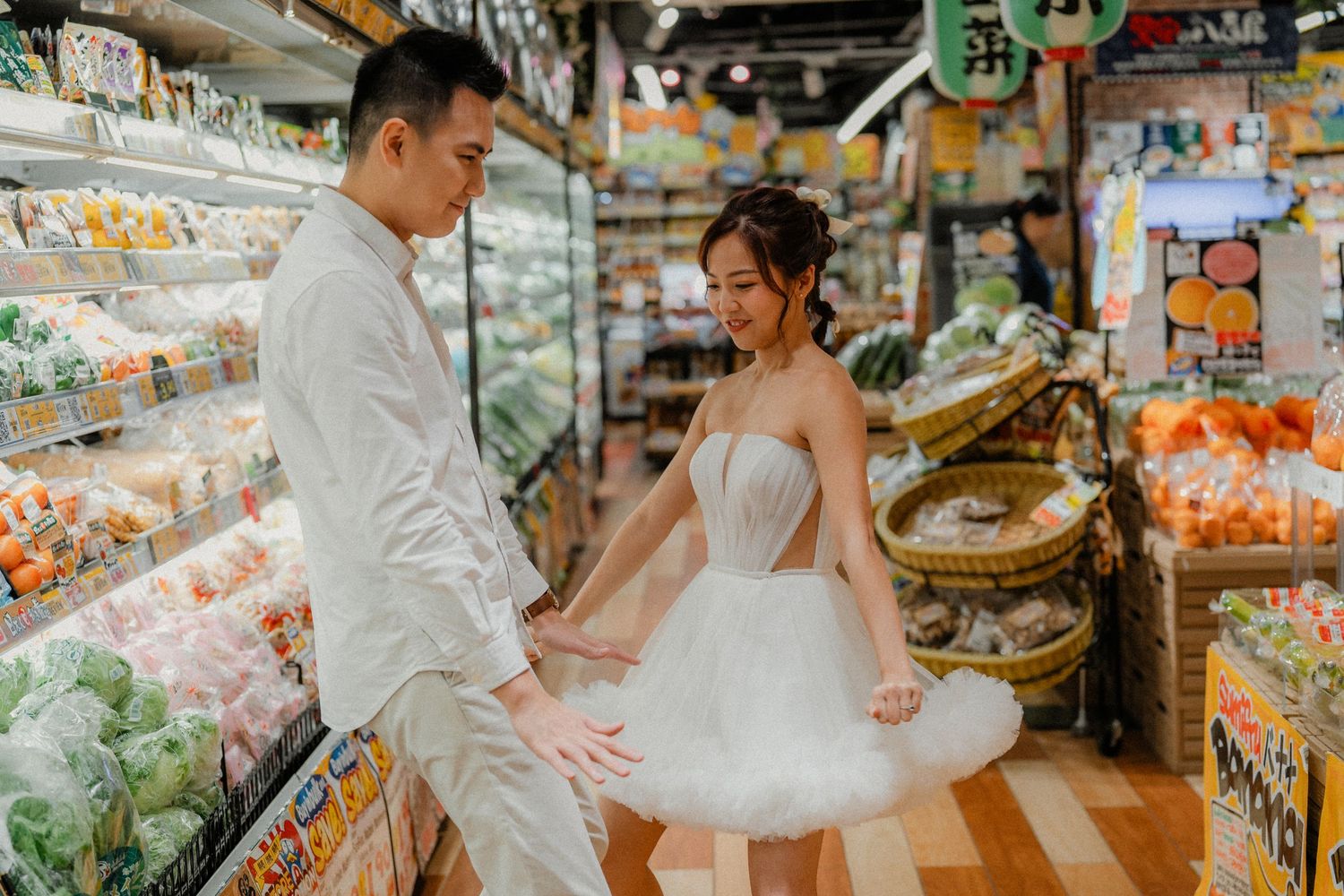 Wedding couple poses playfully between grocery aisles filled with fresh produce.