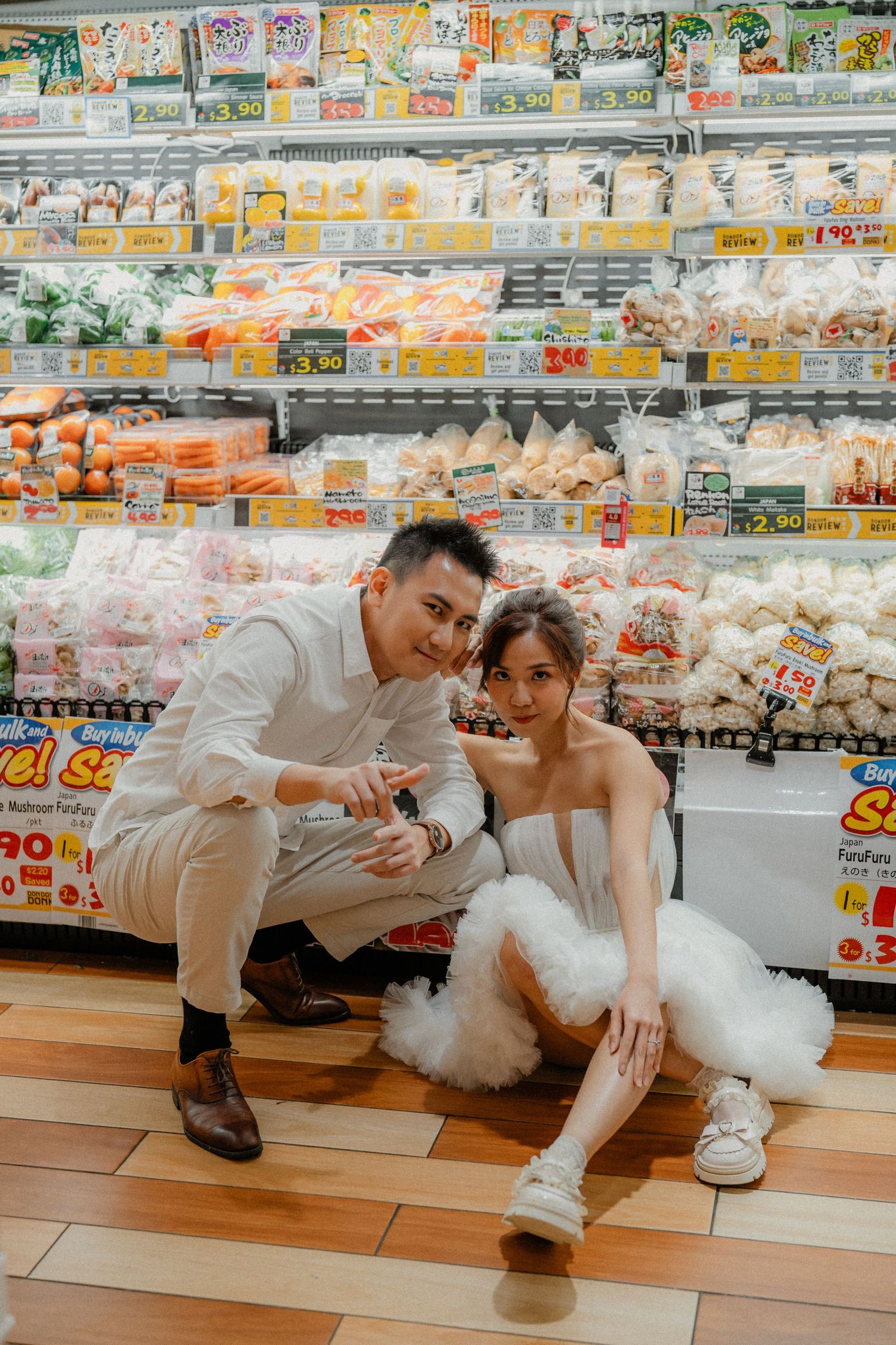 Couple in wedding attire posing casually by frozen food section in grocery store.