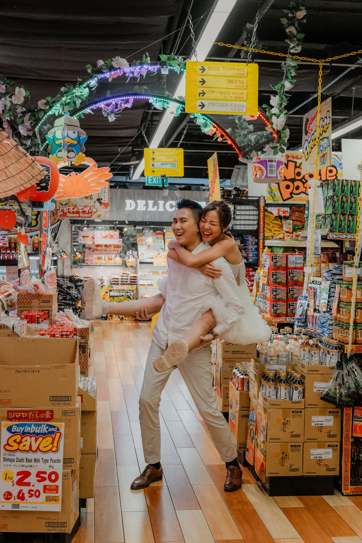 Joyful couple embraces under colorful decorative arch in grocery store.