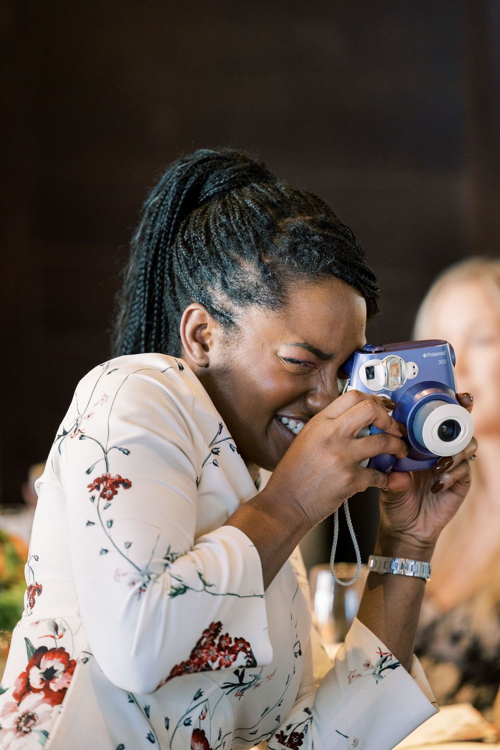 Guest using instant camera at indoor event wearing floral print top.