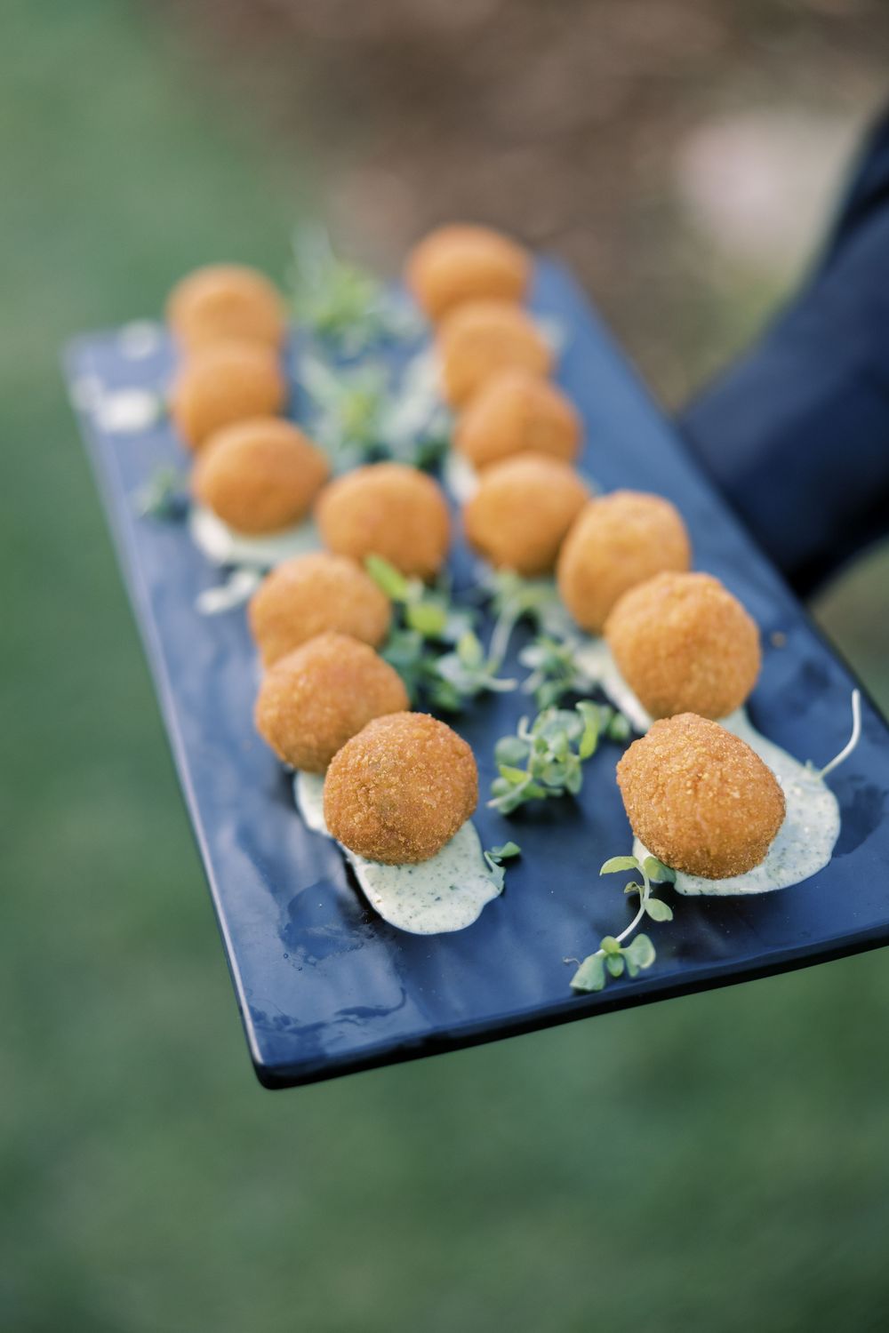 Beautifully plated golden spherical appetizers arranged in a row on a dark plate with fresh herb garnish.