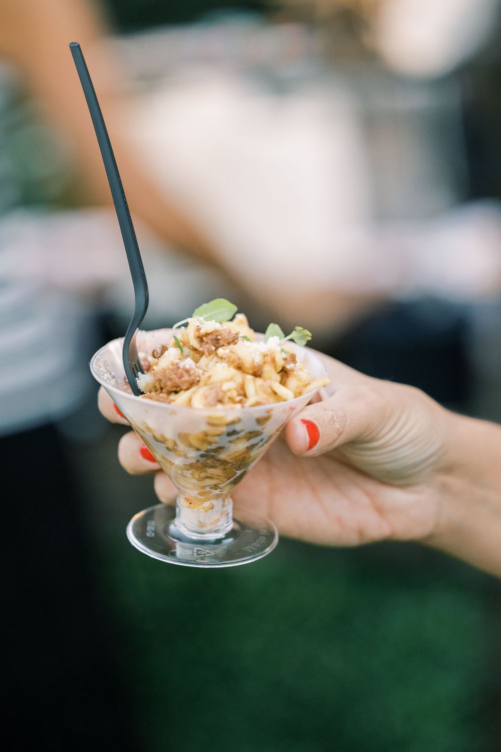 A hand holds a small glass dessert dish filled with creamy pudding topped with crumbled cookies and whipped cream.