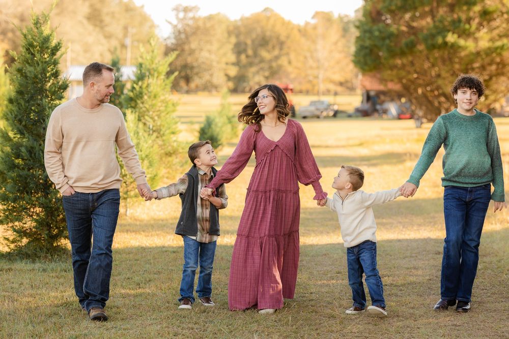 A group walks hand in hand through a golden autumn field with evergreen trees in the background at sunset.