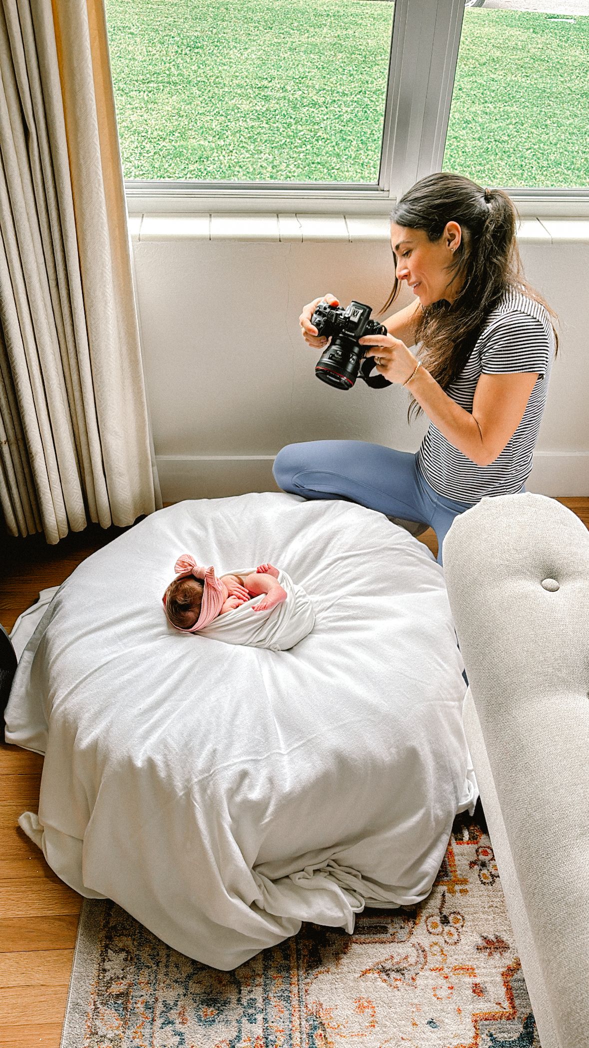 Photographer taking pictures of newborn baby on white cushion by window.