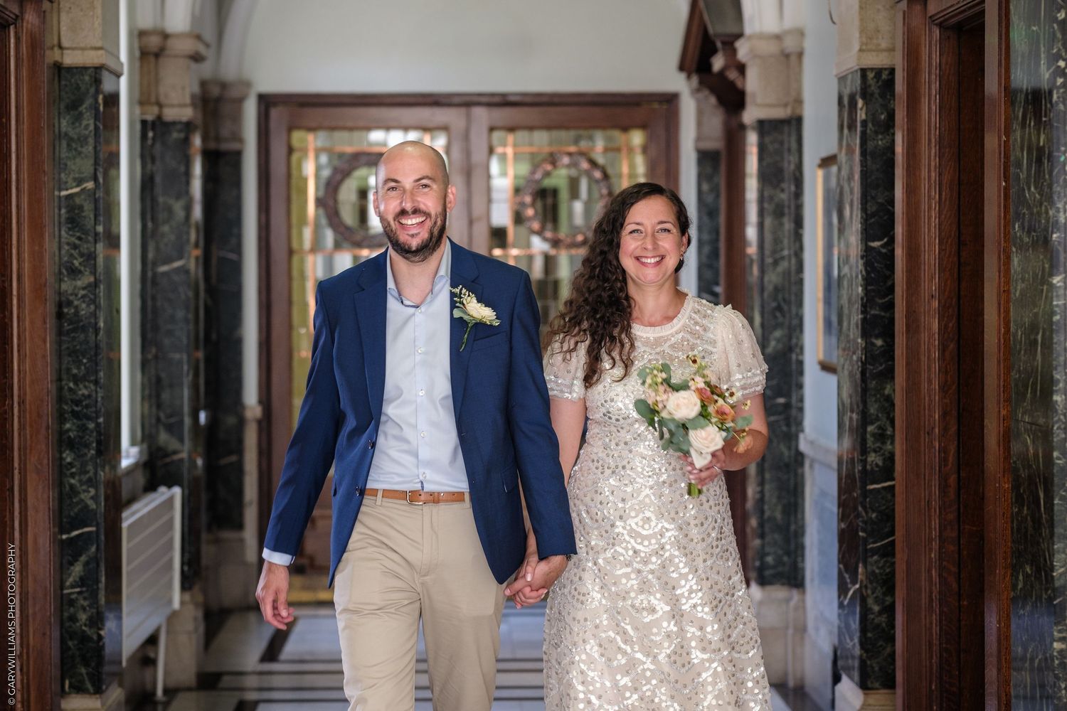Wedding couple exits historic venue through wooden doors while guests throw confetti in celebration.