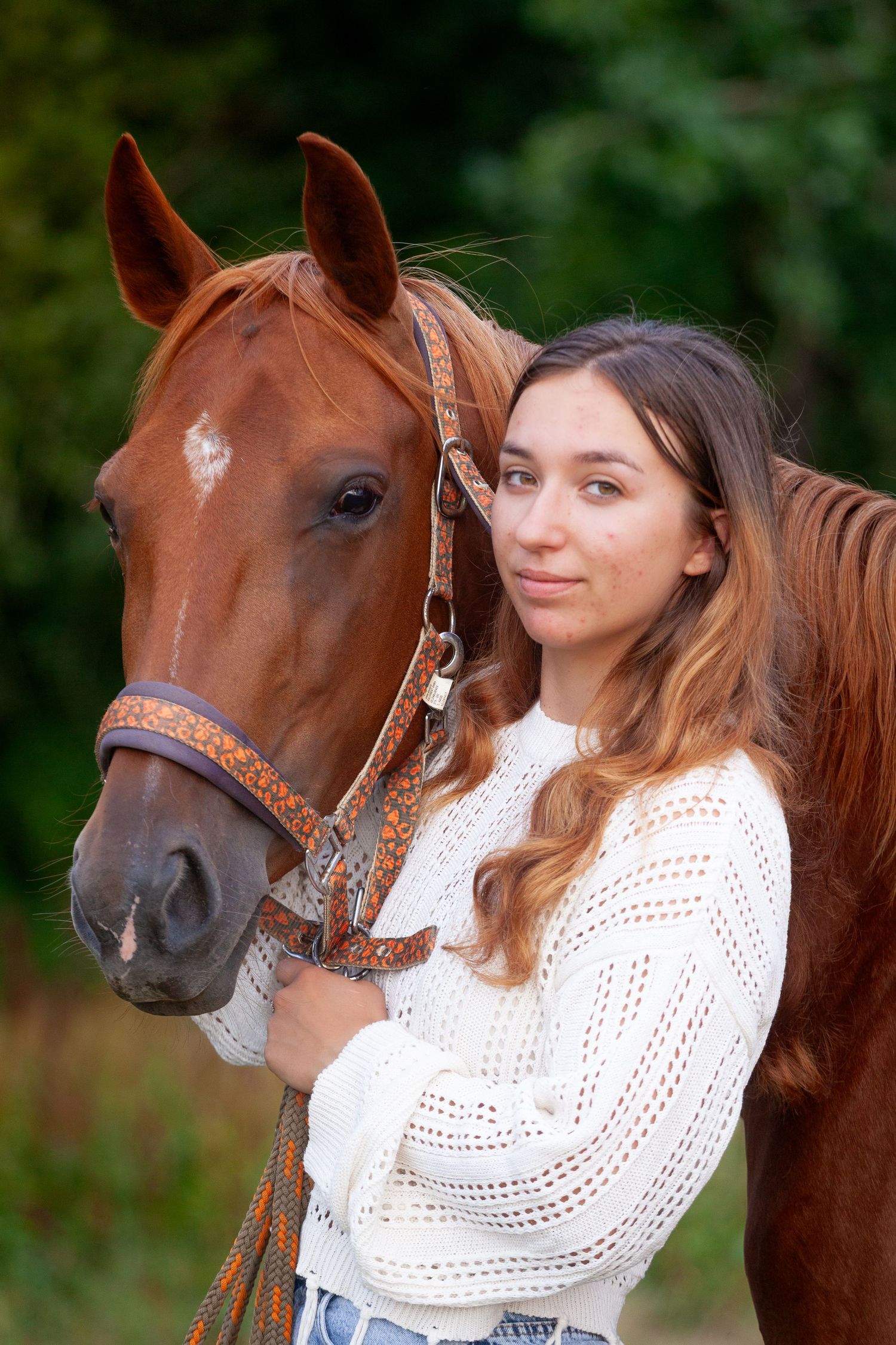 A chestnut horse wearing a decorative bridle stands close to someone in a white crochet sweater.