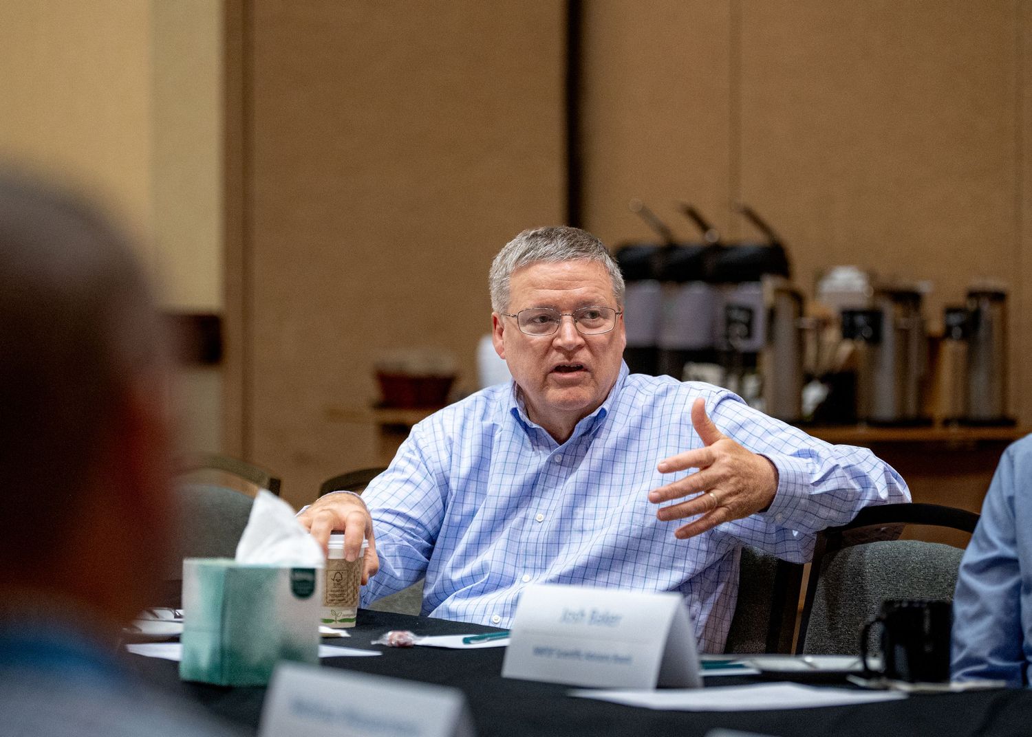 Business meeting participant in blue shirt speaking during discussion.