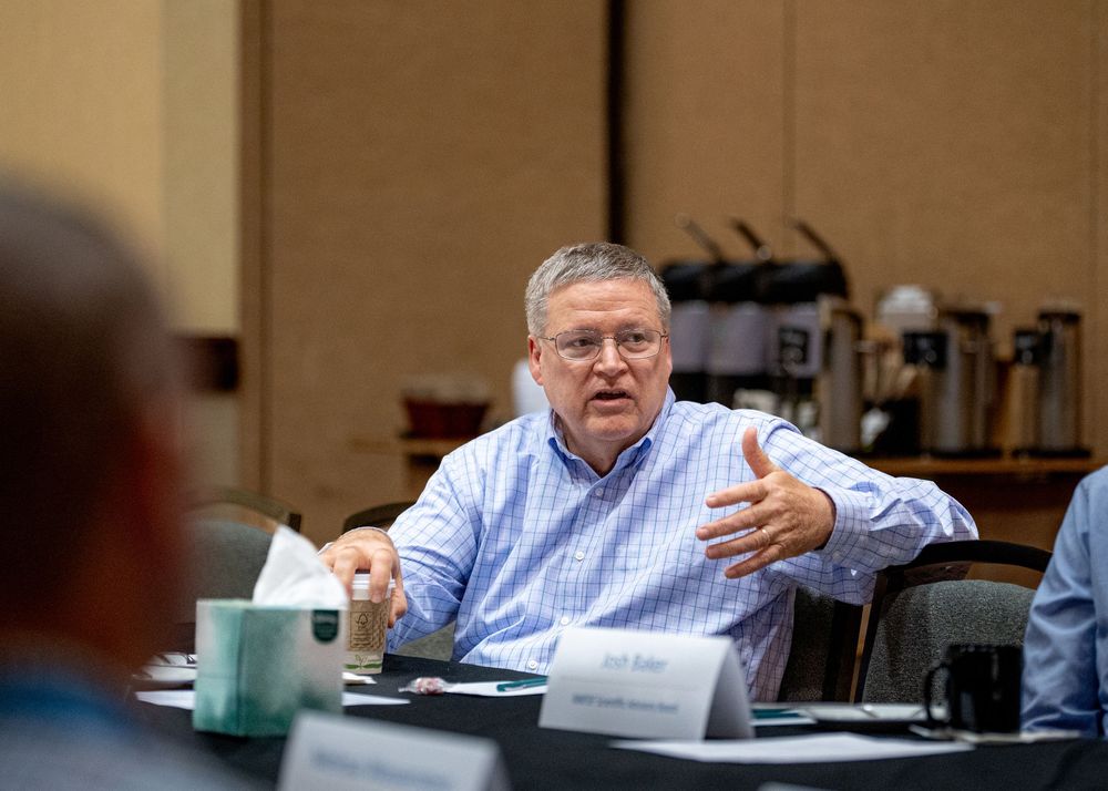 Business meeting participant in blue shirt speaking during discussion.