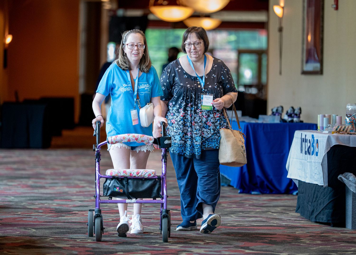 Two attendees walking through a conference hall with one using a mobility aid.
