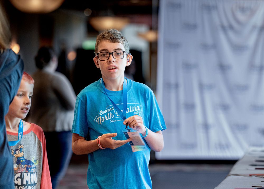 Conference attendee in light blue t-shirt having a discussion during an event.