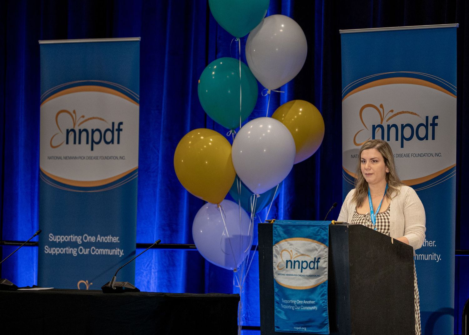 Speaker presenting at NNPDF conference podium with decorative balloons and banners on stage.