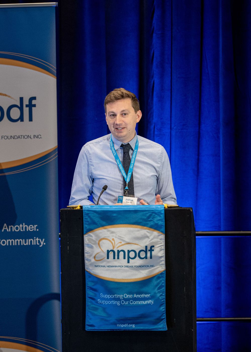 Presenter speaking at NNPDF podium with organizational banner displayed behind them.