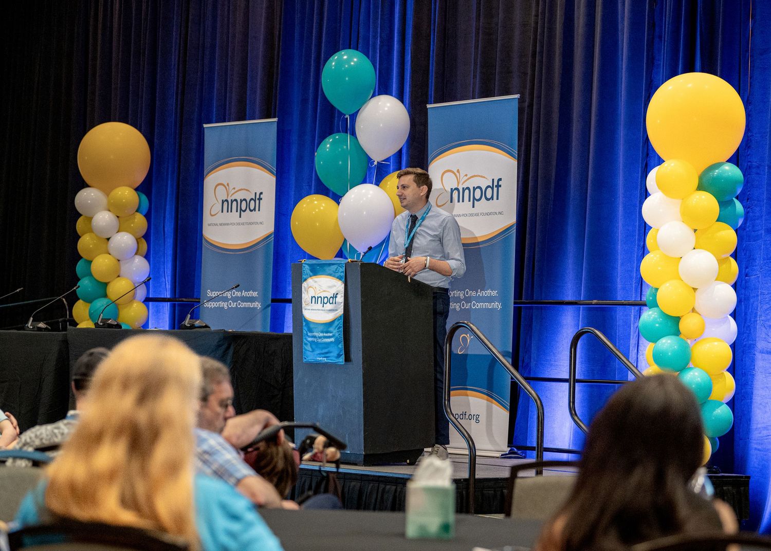 Conference presenter speaking at podium with balloon columns and NNPDF banners decorating the stage.