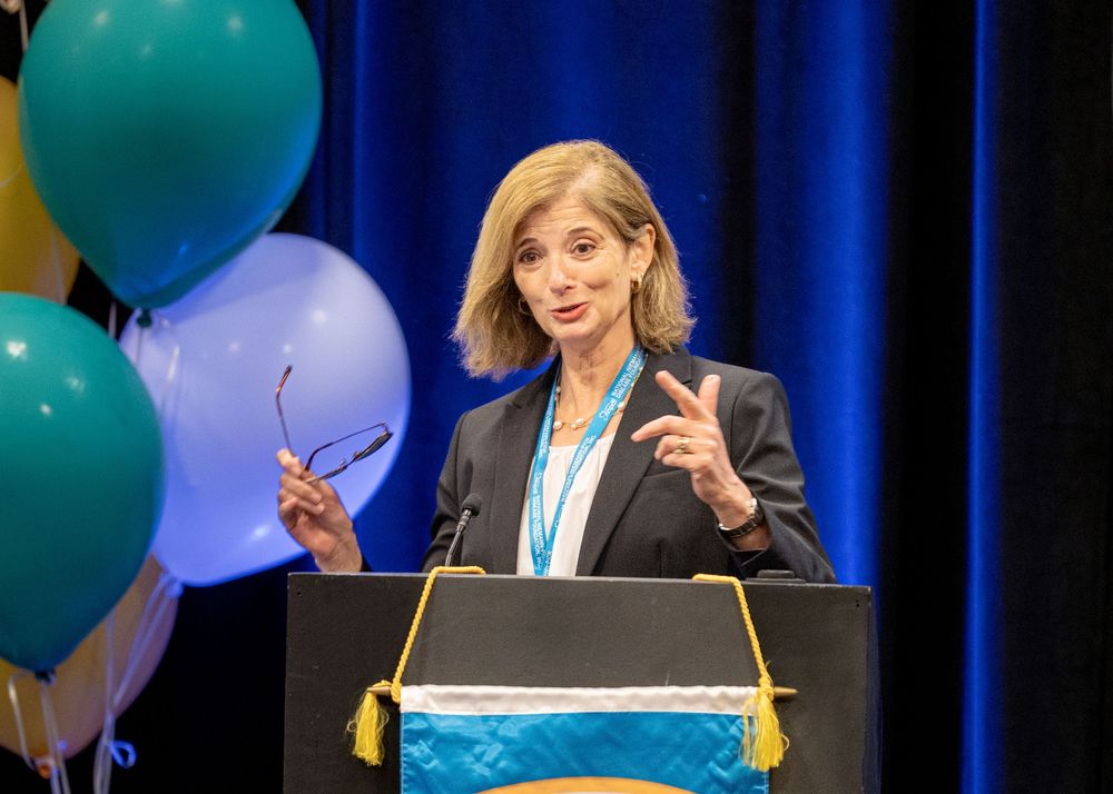 Professional speaker gesturing while delivering presentation at NNPDF conference podium.