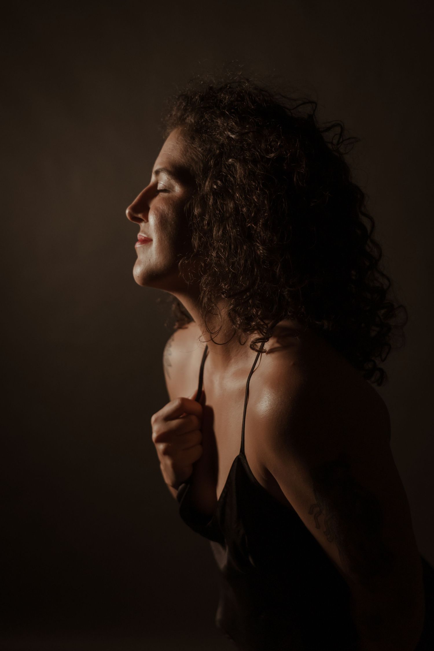 Artistic silhouette portrait showing curly hair against dark moody background.