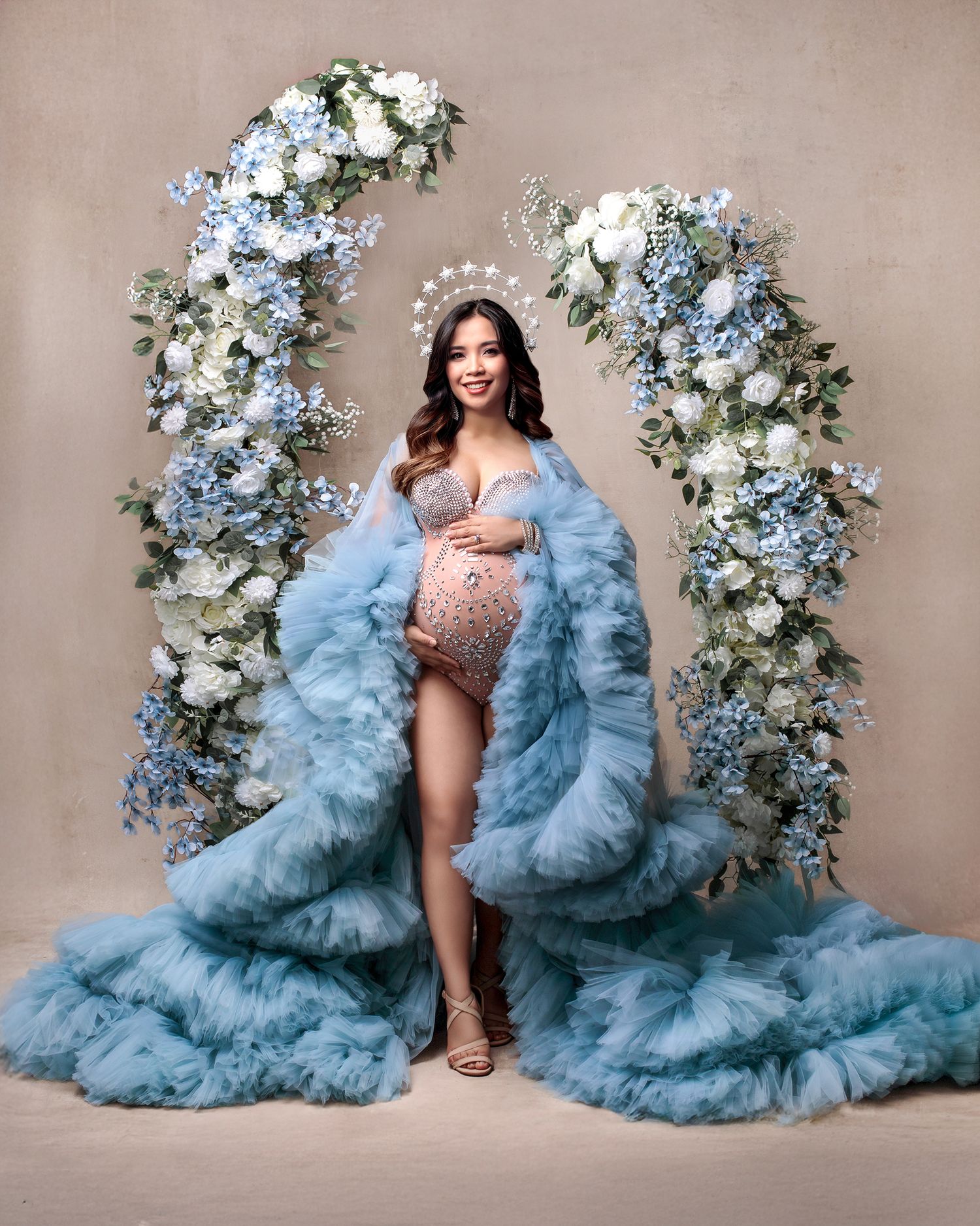 Couture dress maternity session: mum in blue gown against luxurious hand painted backdrop and flower stands.