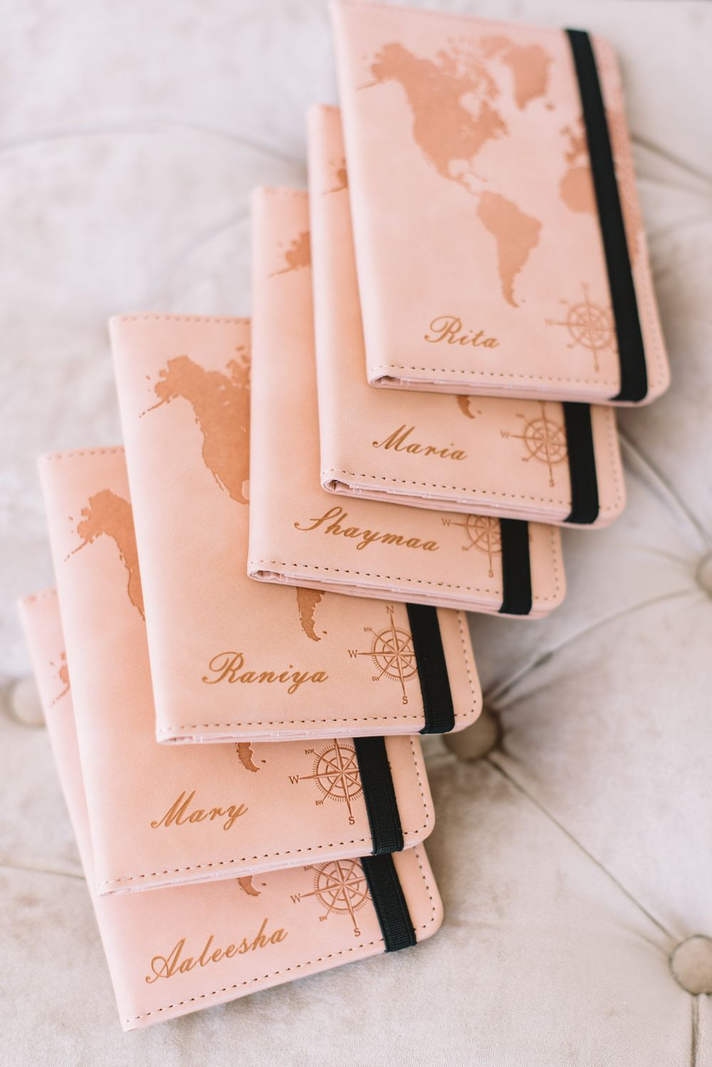 Stack of pink leather passport holders with world map design and custom names engraved.