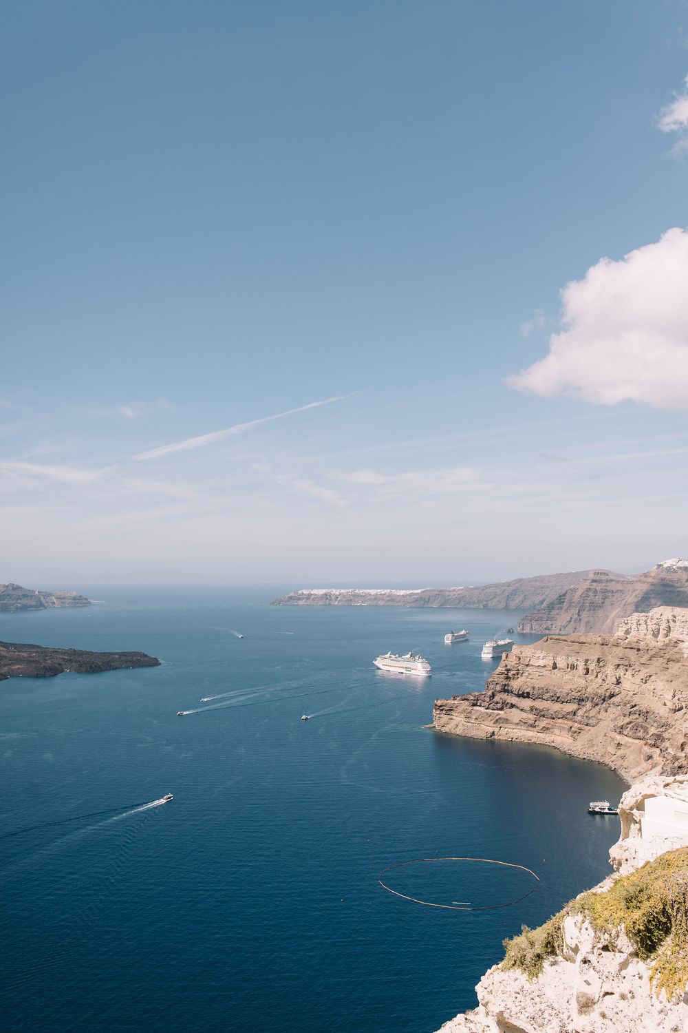 Aerial view of Santorini's caldera with white cruise ships and boats navigating the deep blue Mediterranean waters.
