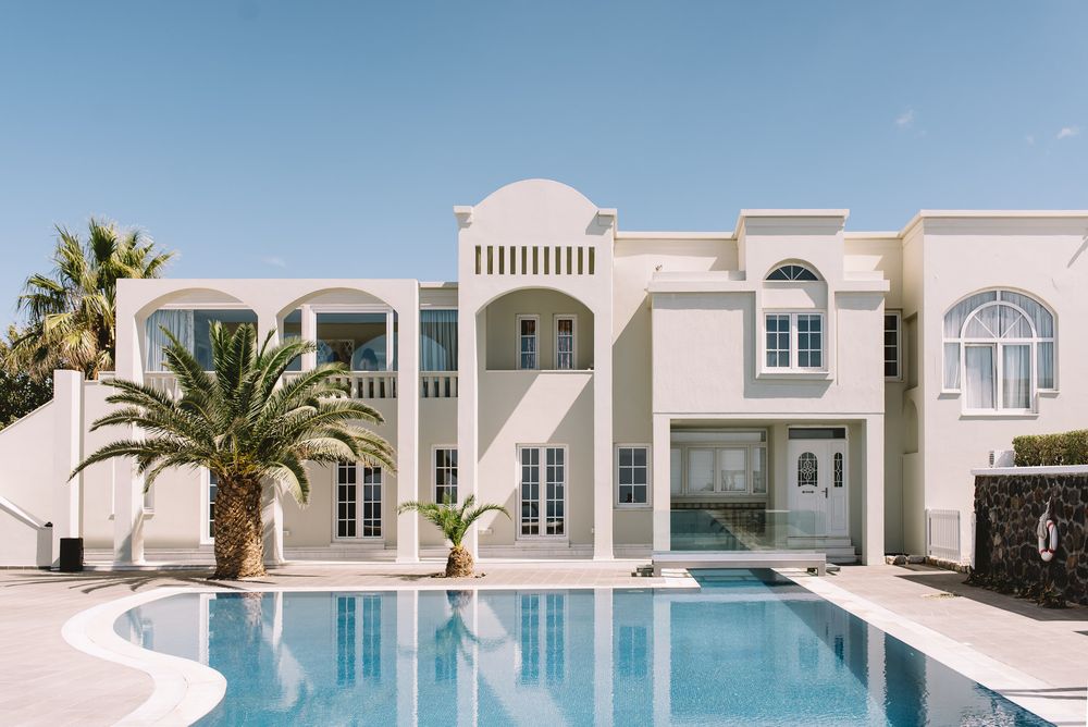 Modern white Mediterranean villa with palm trees and turquoise pool reflecting tranquil luxury lifestyle atmosphere.