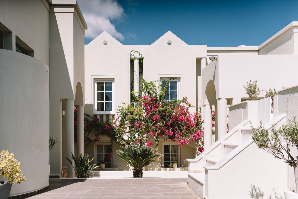 Mediterranean-style white stucco courtyard with bright pink bougainvillea and stepped architecture under blue sky.