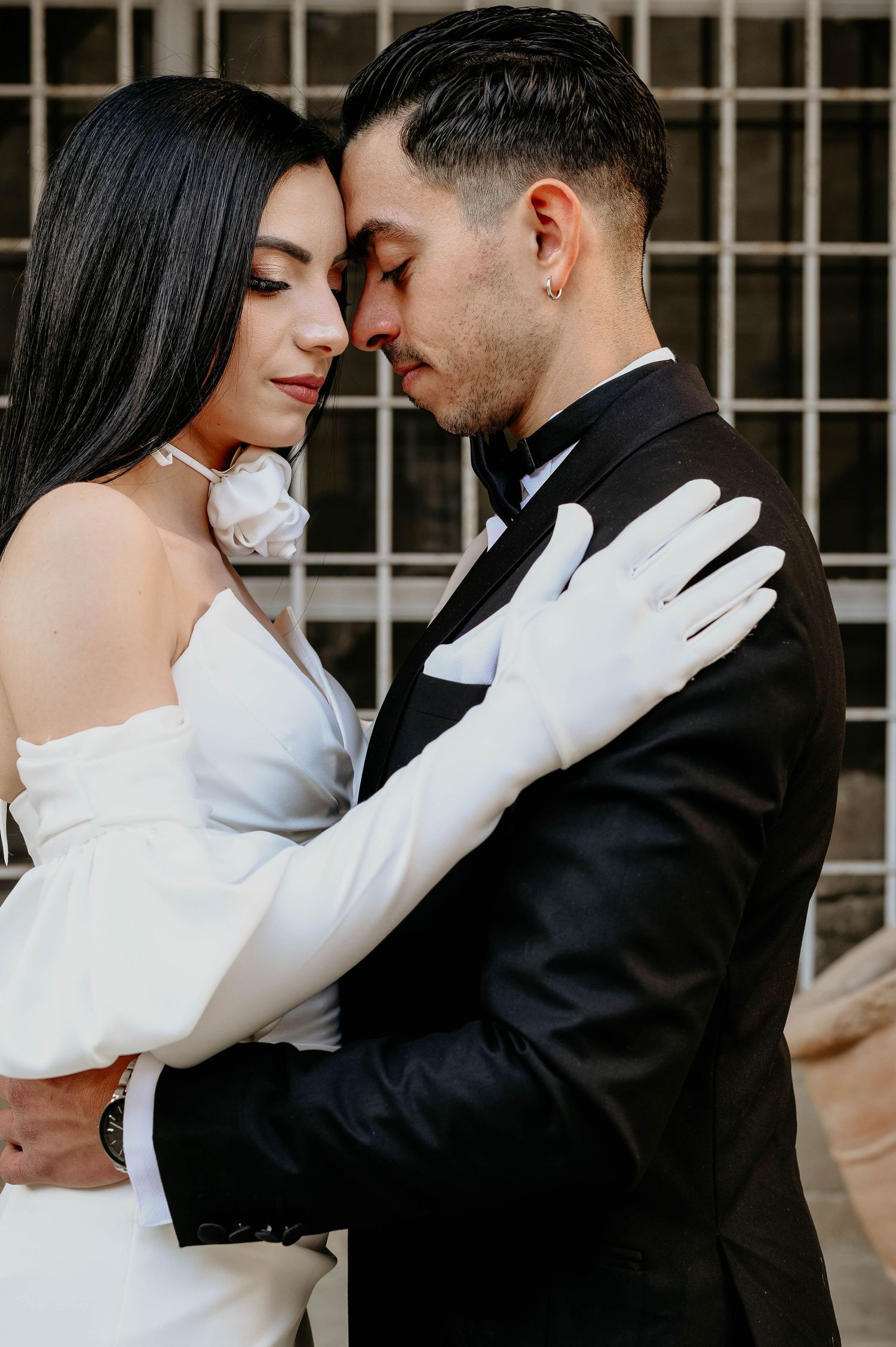 Romantic wedding portrait showing a couple embracing in formal attire with the bride in white and groom in black tuxedo.