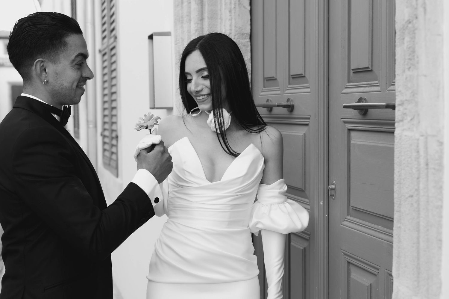 Elegant black and white photo of wedding couple laughing together in front of arched doorways.