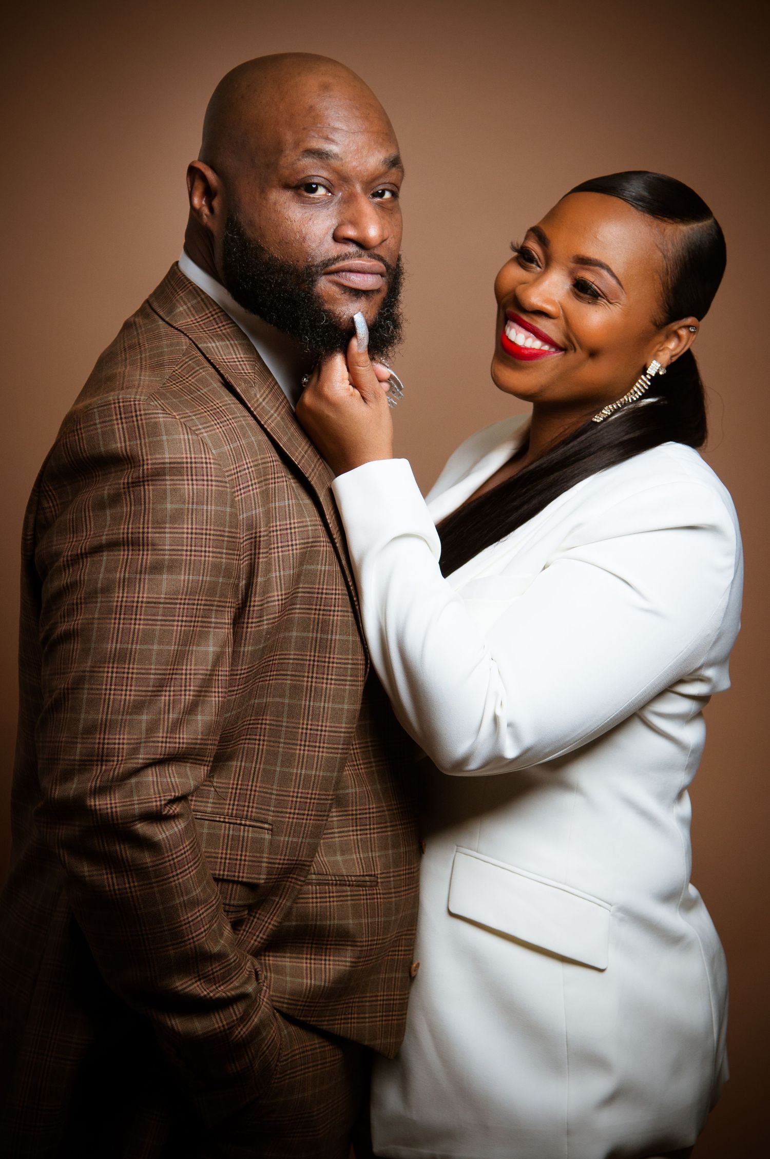 Romantic couple shares intimate moments in brown and white formal wear against mocha backdrop in professional photo series.