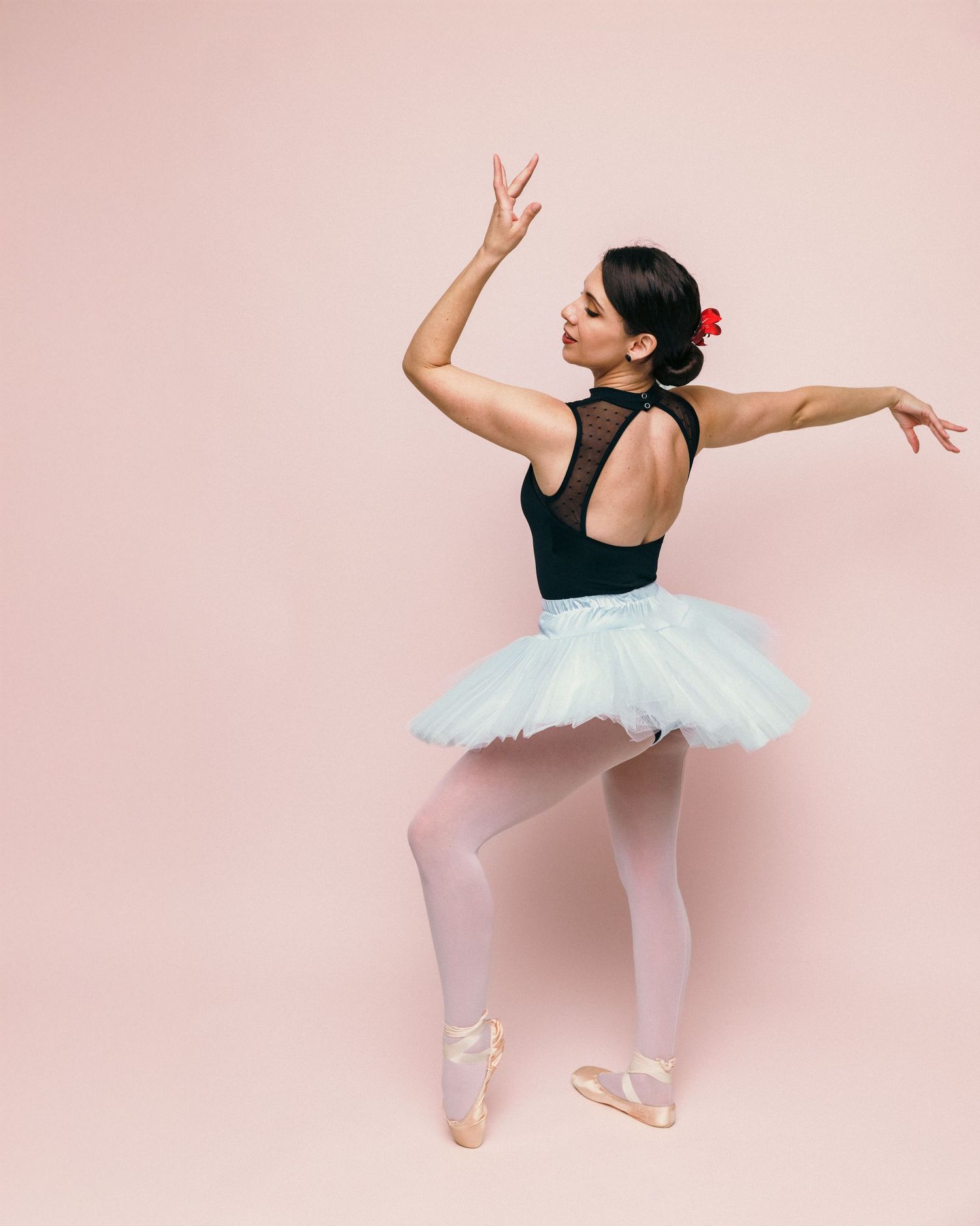 Ballet dancer in white tutu and black leotard poses gracefully against pink background.