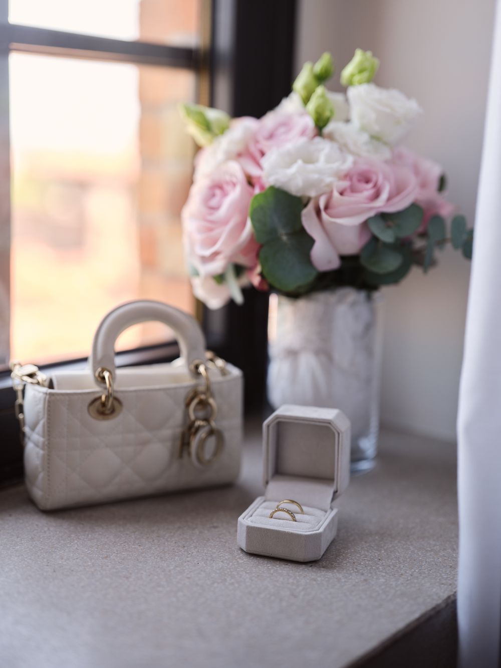 Wedding accessories including pink roses in vases and a ring box displayed on a gray surface. Photoshoot by Venice Photographer Alina Indi