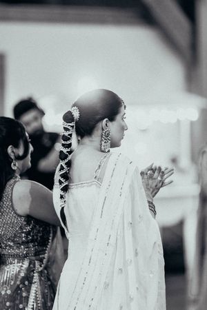 Traditional Indian wedding hairstyle with jasmine flowers woven into long braid, wearing white sari with delicate details.