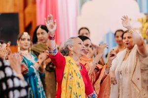 A group of people in colorful traditional attire raise their hands during a cultural celebration with vibrant decorations.