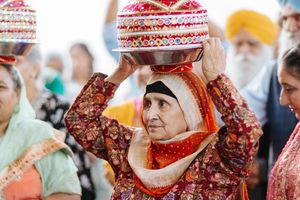 Traditional Sikh bride performs kalash ritual wearing red and gold attire during wedding ceremony.