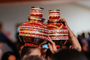 Traditional Indian wedding kalash vessels decorated with red and gold patterns held up during a ceremony.