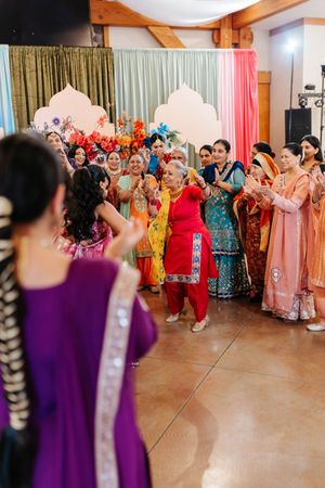 A group of people in colorful traditional outfits dance and celebrate at a cultural wedding reception.