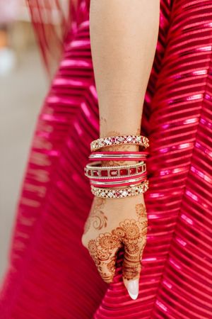 Close-up view of traditional Indian bridal bangles and henna adorned hand against a red background.