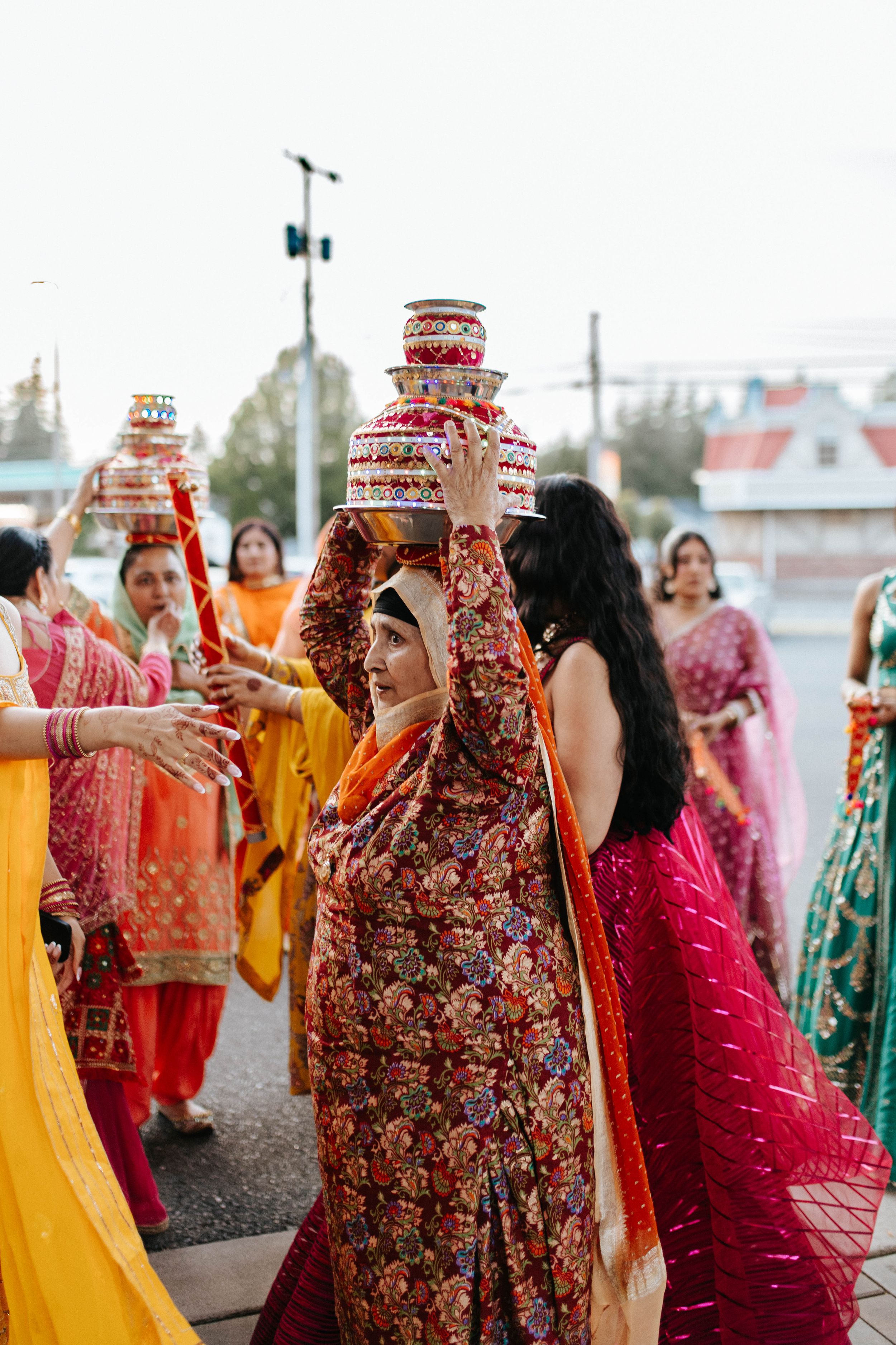 Guests in traditional Indian attire participate in a wedding ceremony ritual balancing ornate pots during celebrations.