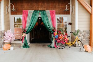 A panoramic view of a rustic venue interior decorated with pink and teal curtains and vintage-style event decor.