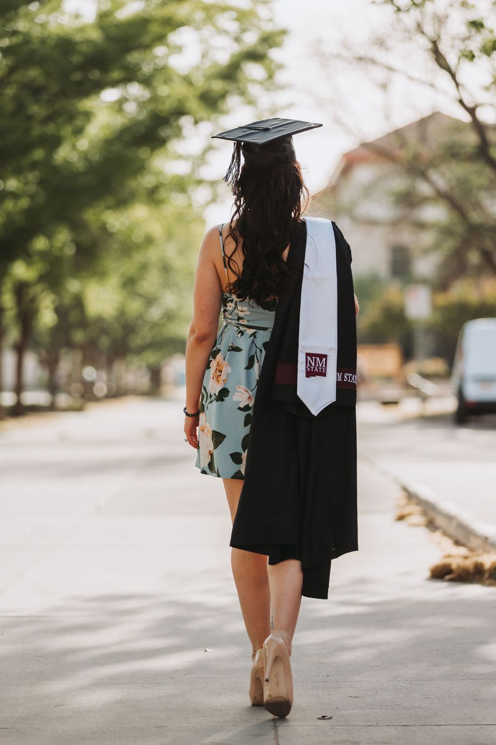 Someone wearing casual dress shorts walks down a sunny sidewalk carrying a black tote bag.