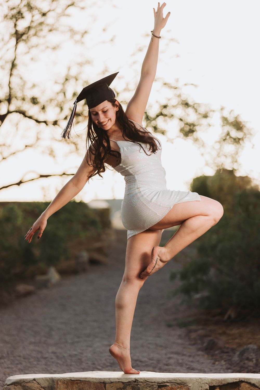 Dancer in white dress performs graceful dance movements on outdoor path at dusk with glowing natural light.