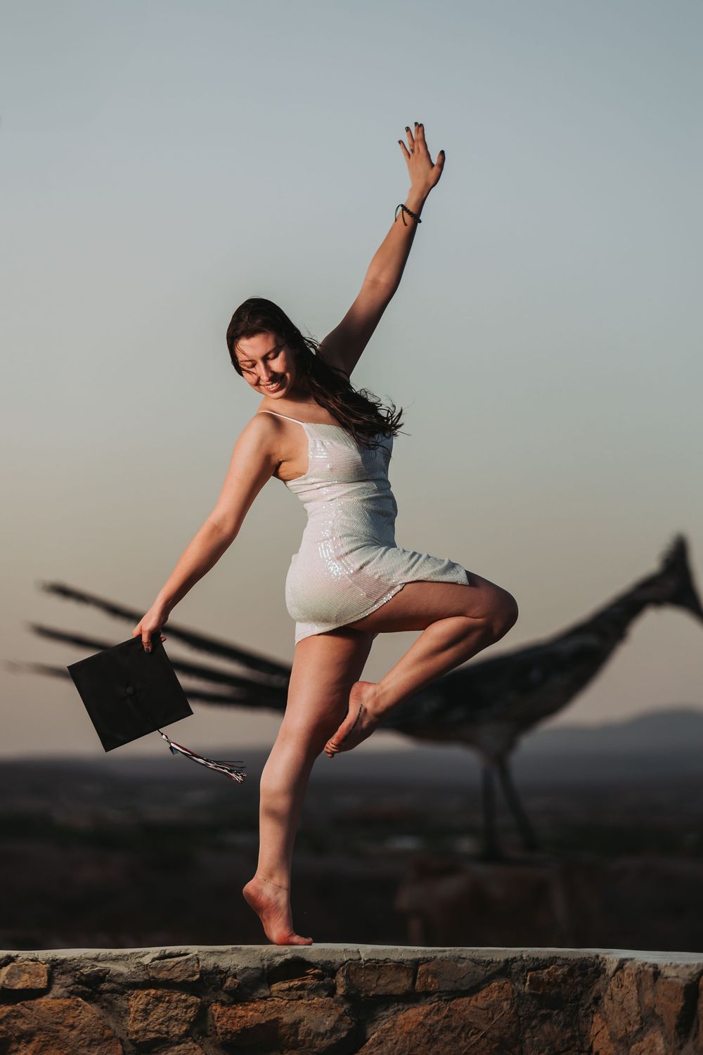A dancer in white performs a dramatic leap sequence against a sunset sky on rocky terrain.
