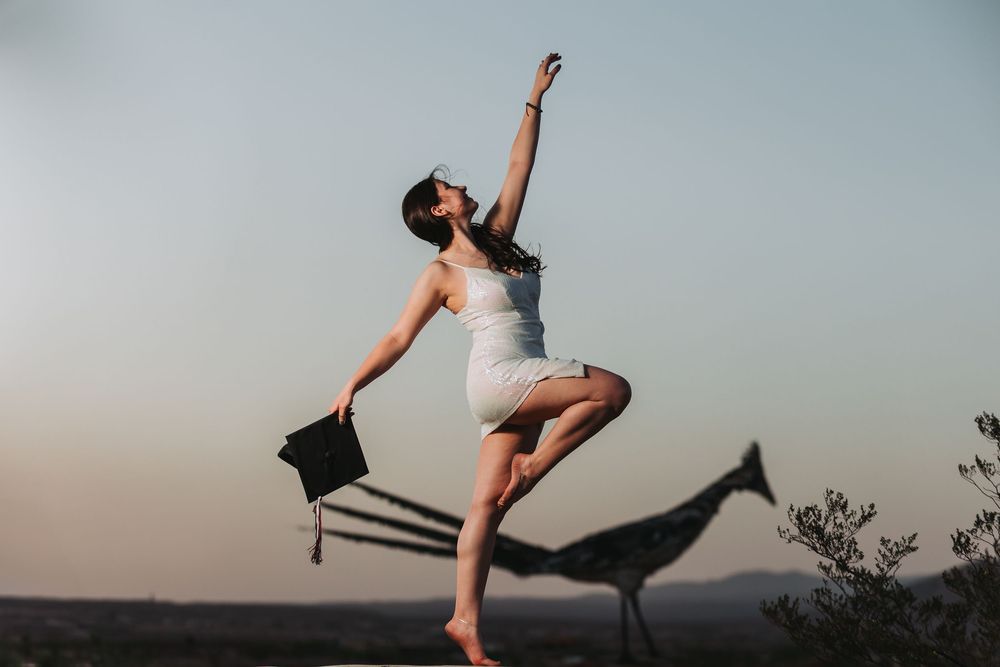 A dancer in white performs a graceful leap against a sunset sky with mountains in the background.