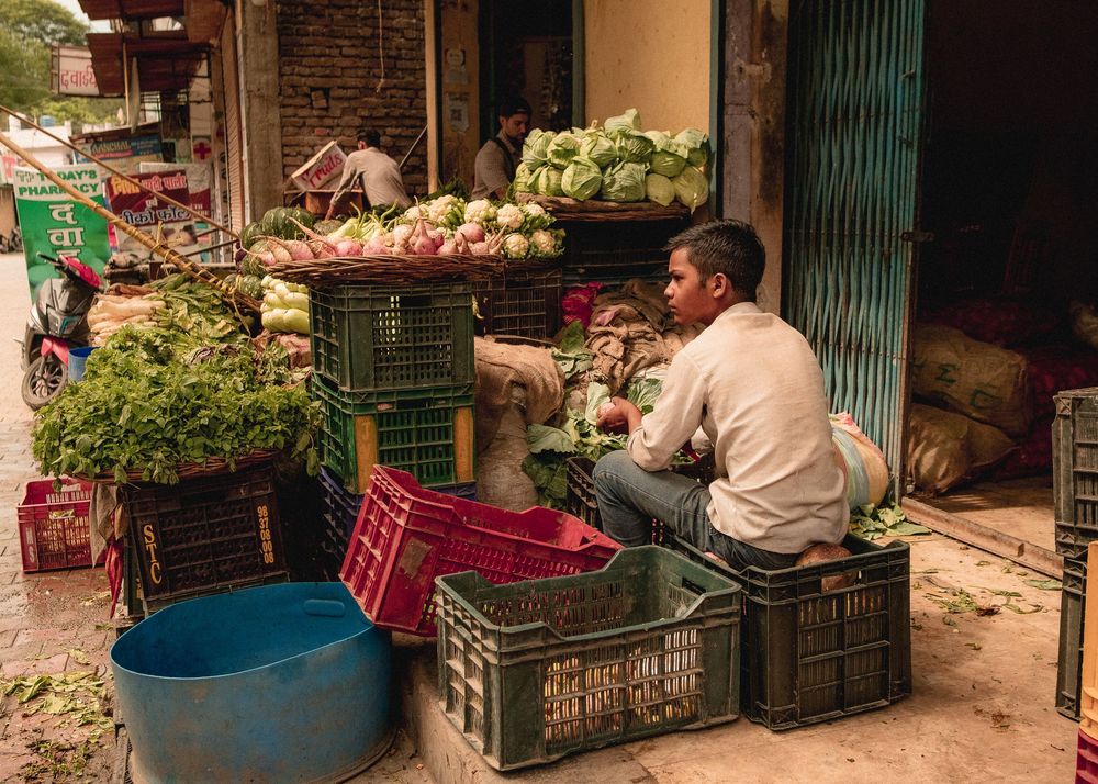 Vegetable vendor arranging produce in plastic crates at a local market.